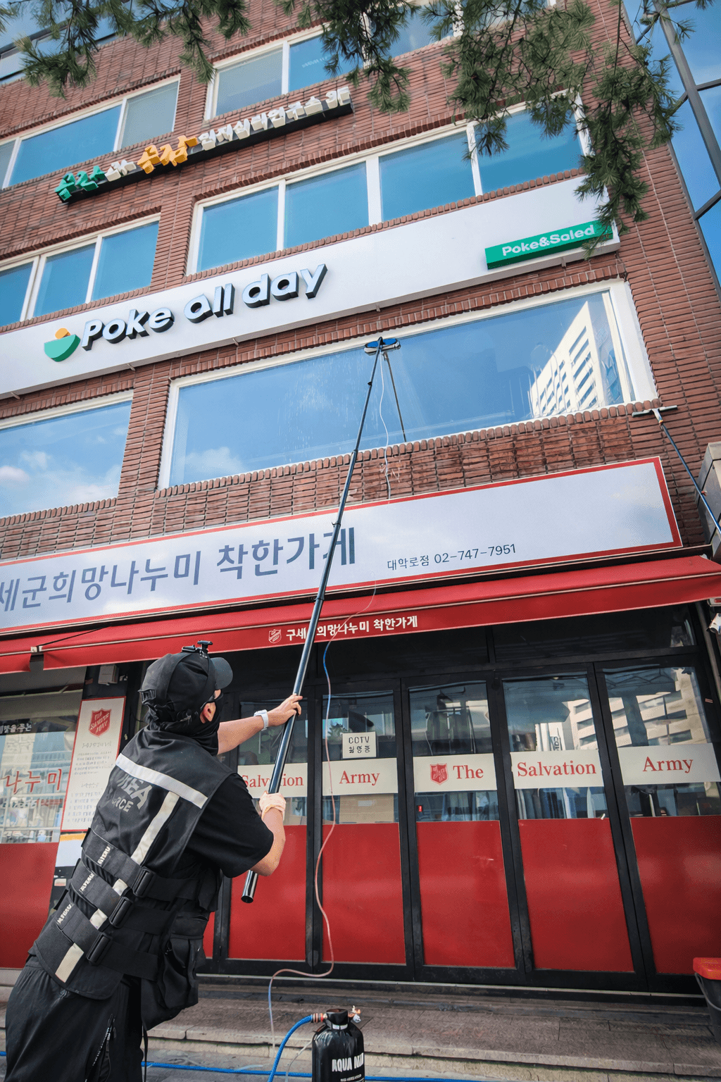 상가 전면 유리를 폴 장비로 청소하는 작업자